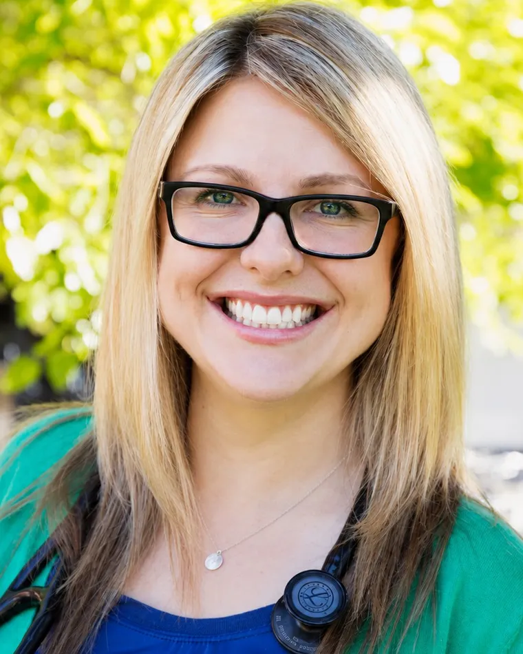 Dr. Jaclyn Perchaluk, ND, smiling outdoors among green leaves