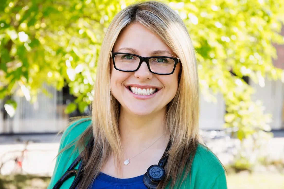 Dr. Jaclyn Perchaluk, ND, smiling outdoors among green leaves